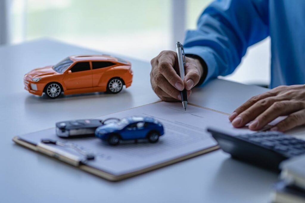 Une personne signe un document à côté de voitures miniatures, illustrant une démarche administrative pour contacter la SAAQ concernant un véhicule au Québec.