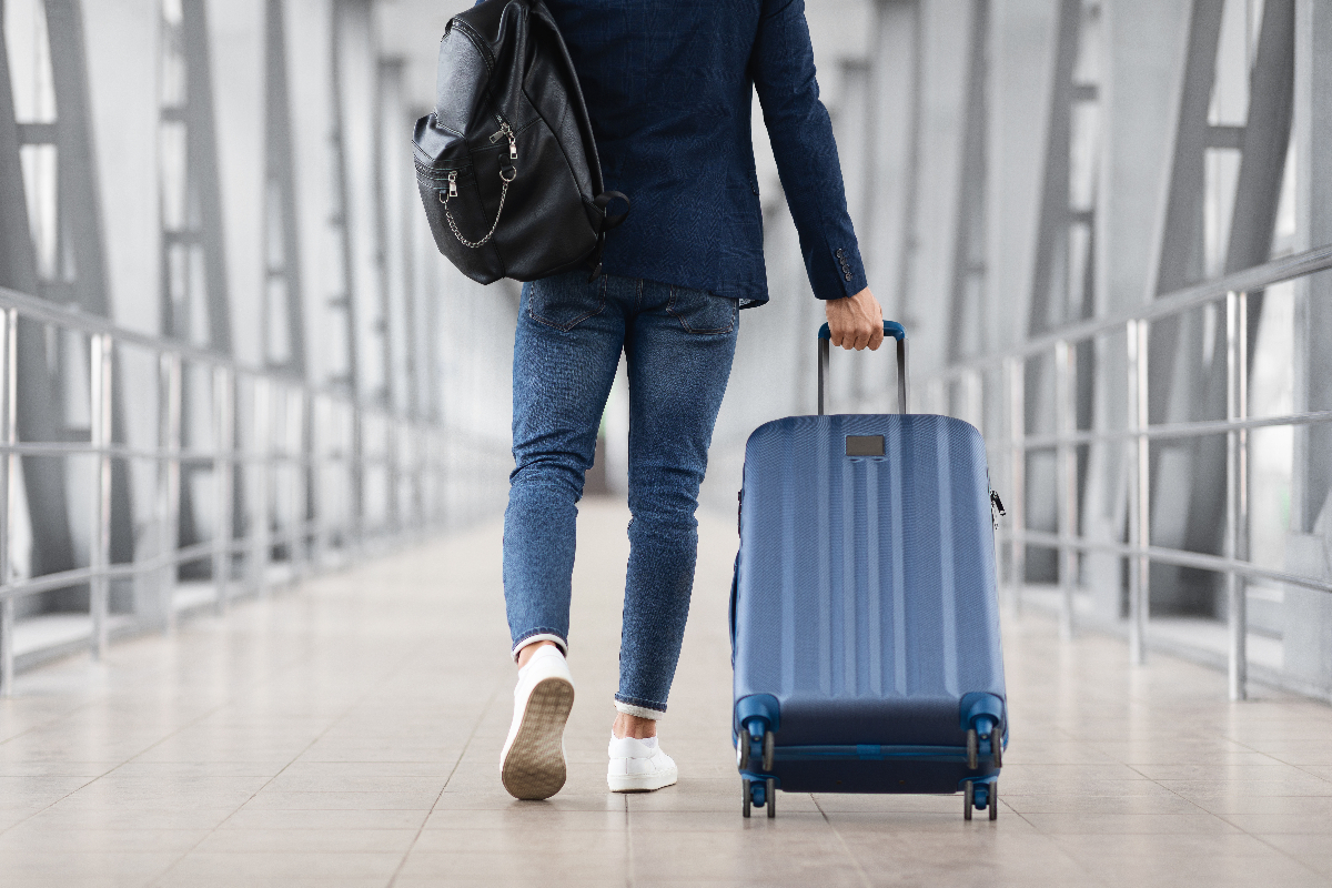 Persona de espaldas con mochila y maleta de ruedas en un pasillo
